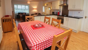 A compact kitchen with white cabinets, a microwave, and a stove. There is a dining area with a red and white checkered tablecloth and wooden chairs. - 63 Moinin (Kilkee)