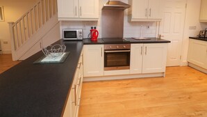 A modern kitchen with white cabinets, a black countertop, a stainless steel range hood, and a microwave. - 63 Moinin (Kilkee)