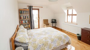 Ein Schlafzimmer mit einem Bett, einem Bücherregal, einem Sessel, einem Fernseher und einem Fenster.