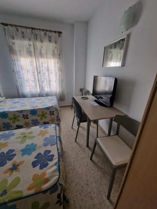 Una habitación con cama, escritorio, silla y televisor.