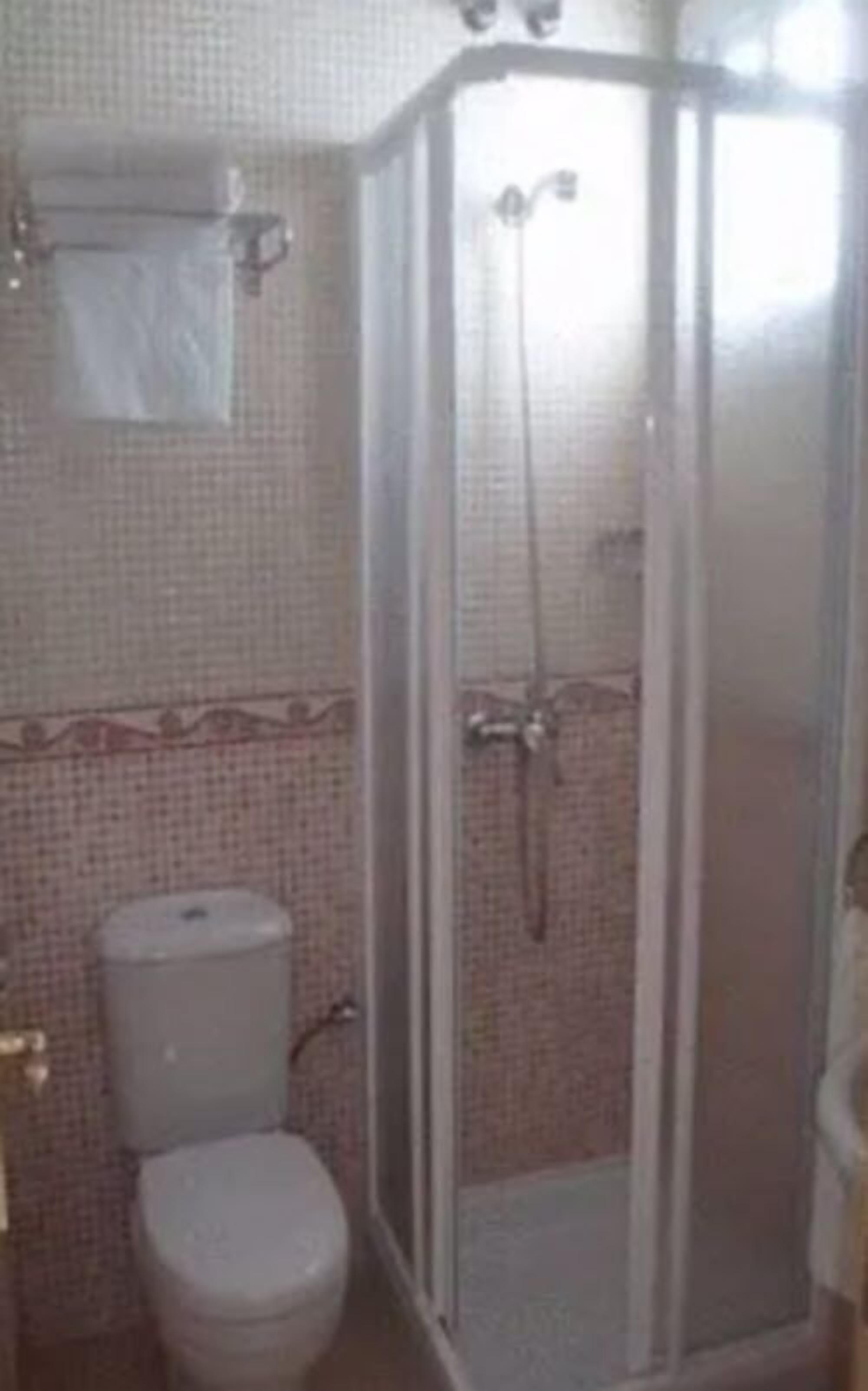 Un baño con inodoro, cabina de ducha y pared de azulejos.
