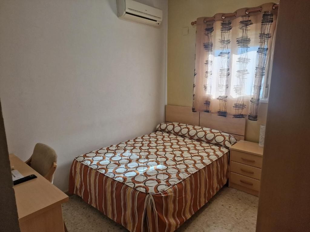 Un dormitorio con cama, escritorio, silla y ventana con cortinas.
