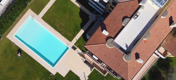 An aerial view of a property with a swimming pool, a covered patio area, and a building with a tiled roof.