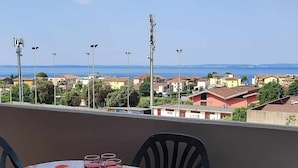 A balcony with a table set for dining, overlooking a coastal town with buildings and a clear sky.
