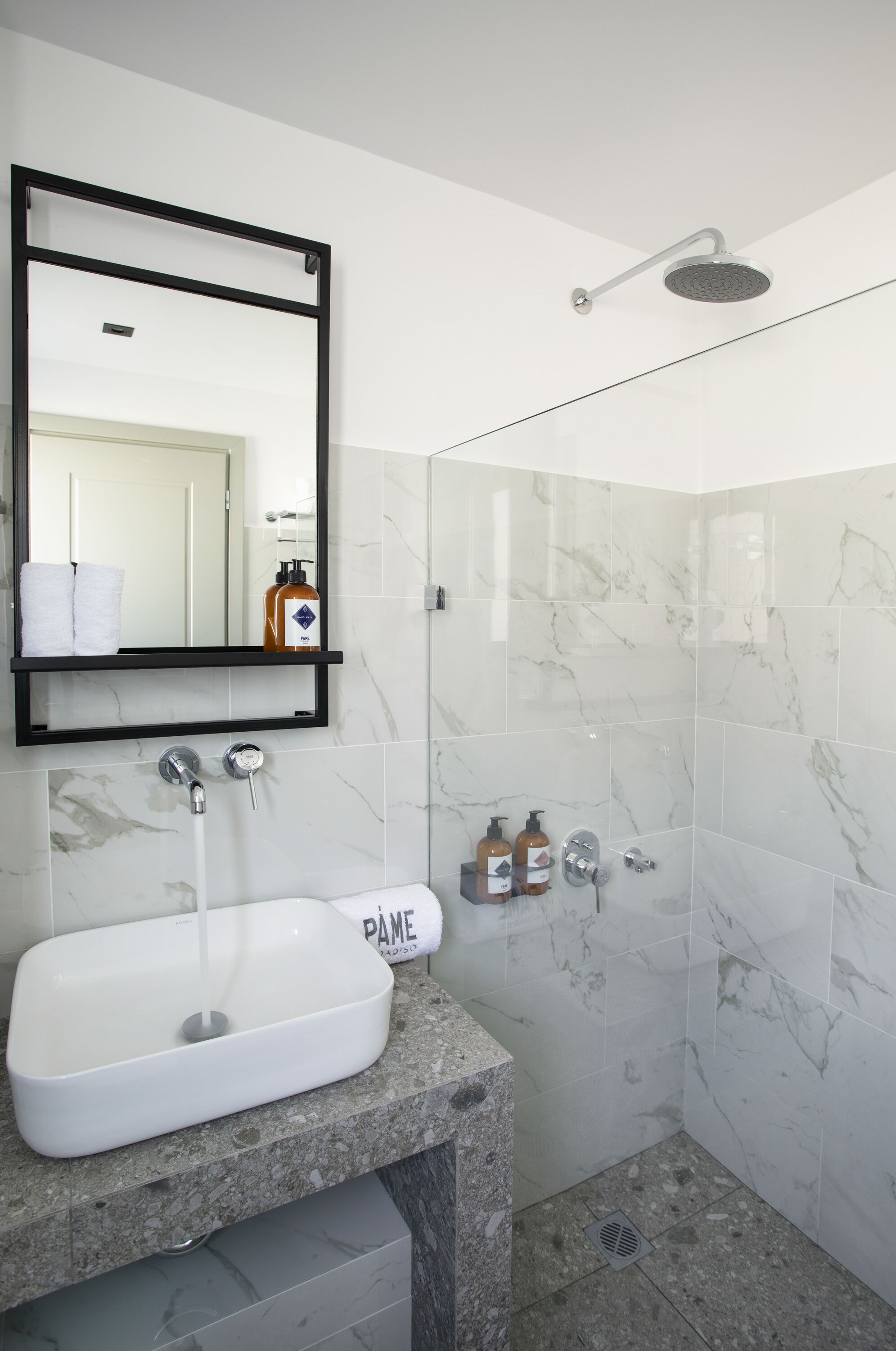 A modern bathroom with a white sink, a mirror, a shower, and marble tiles.