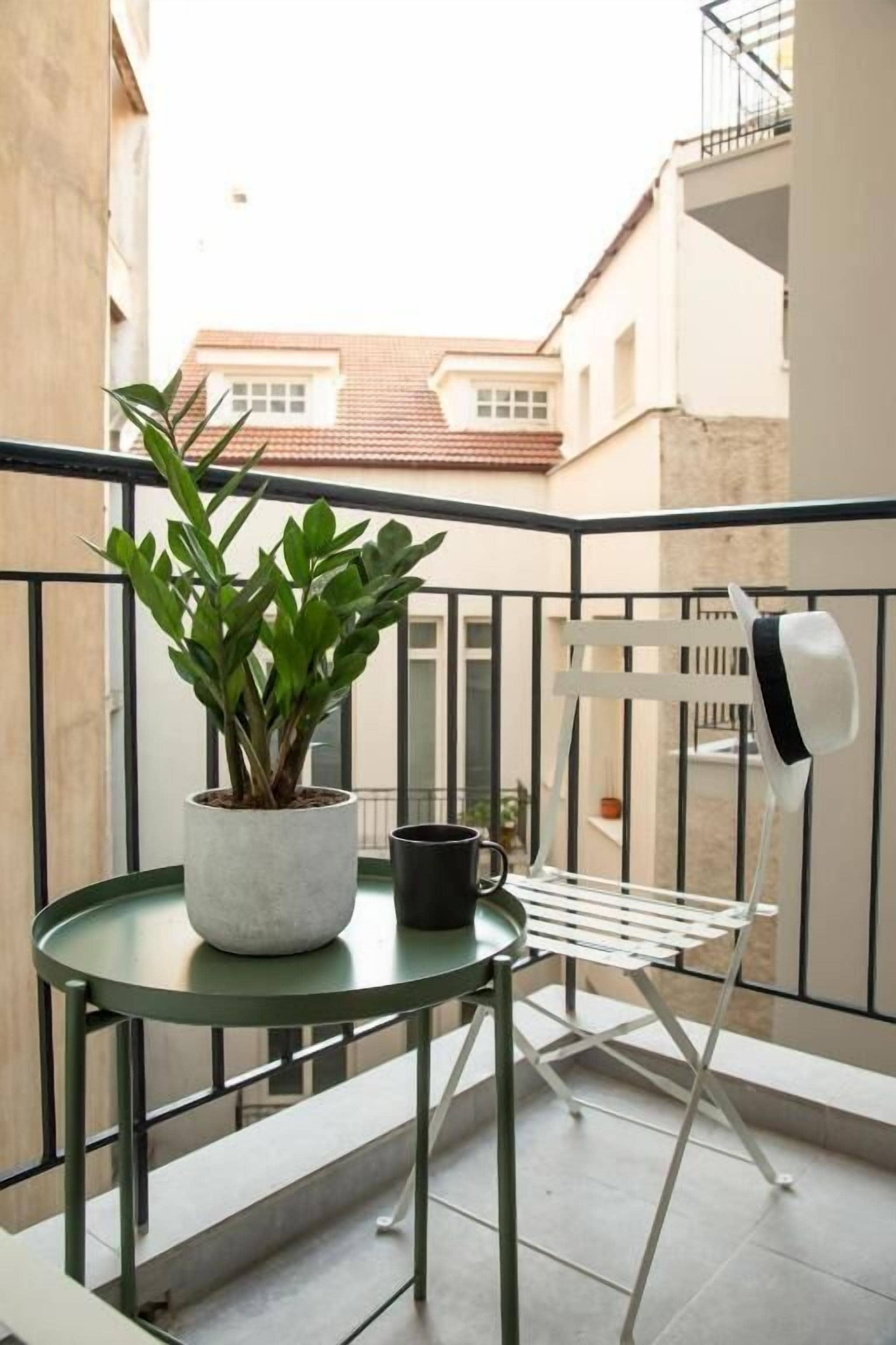 A small balcony with a potted plant, a black mug, and a white chair.