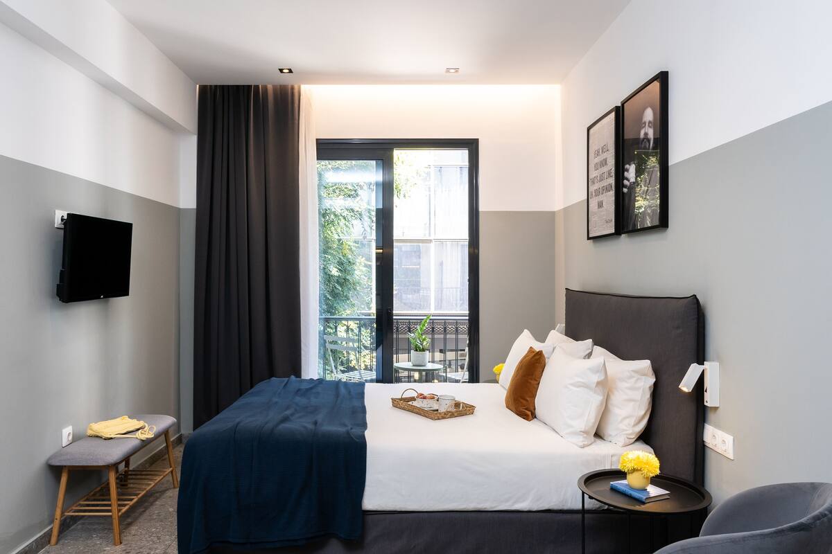 A modern hotel room with a bed, bedside table, and a TV mounted on the wall.
