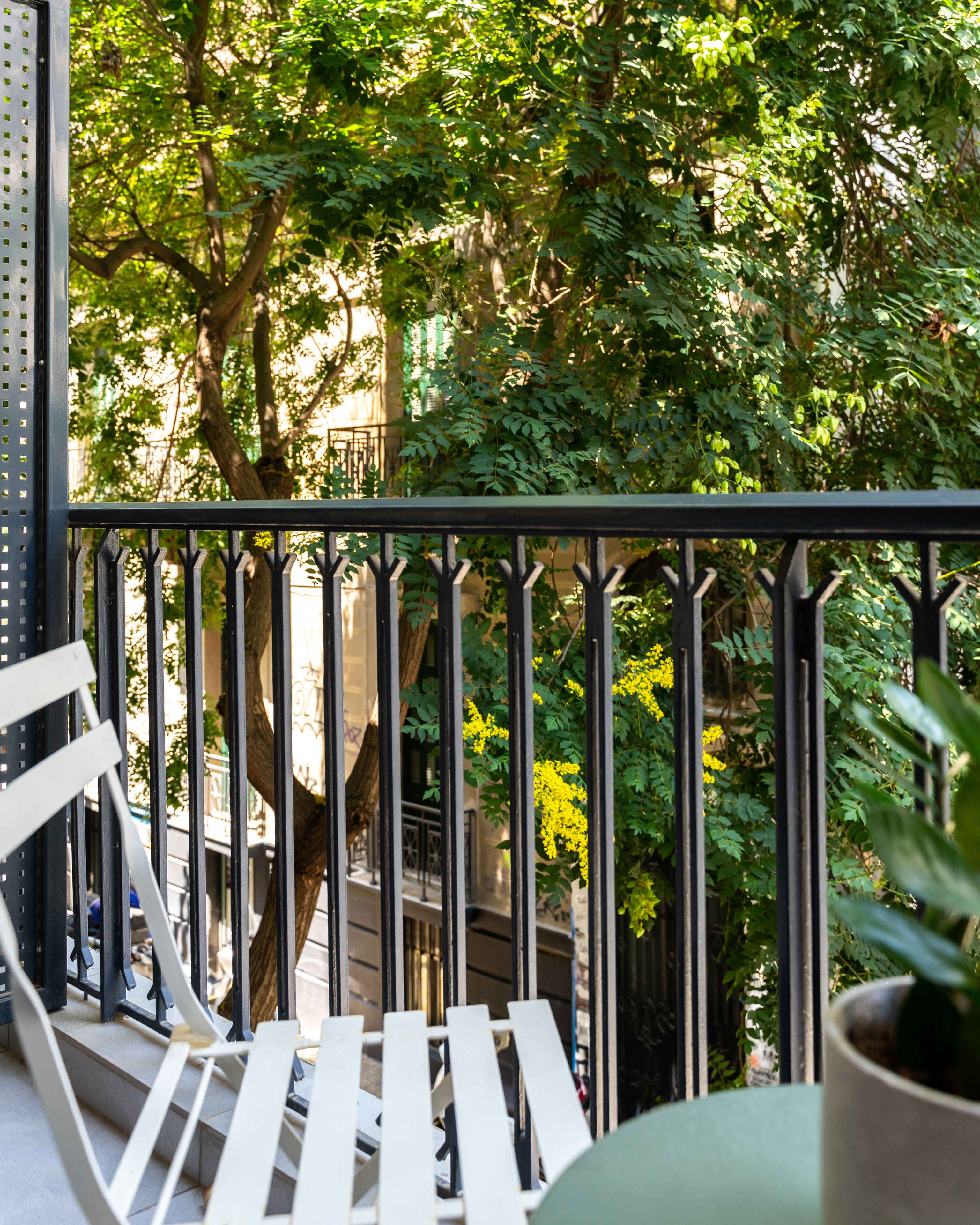 A balcony with a metal railing, white chairs, and a potted plant.