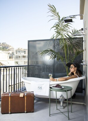 Una bañera con una toalla, una maleta y una mesa con uvas en un balcón.