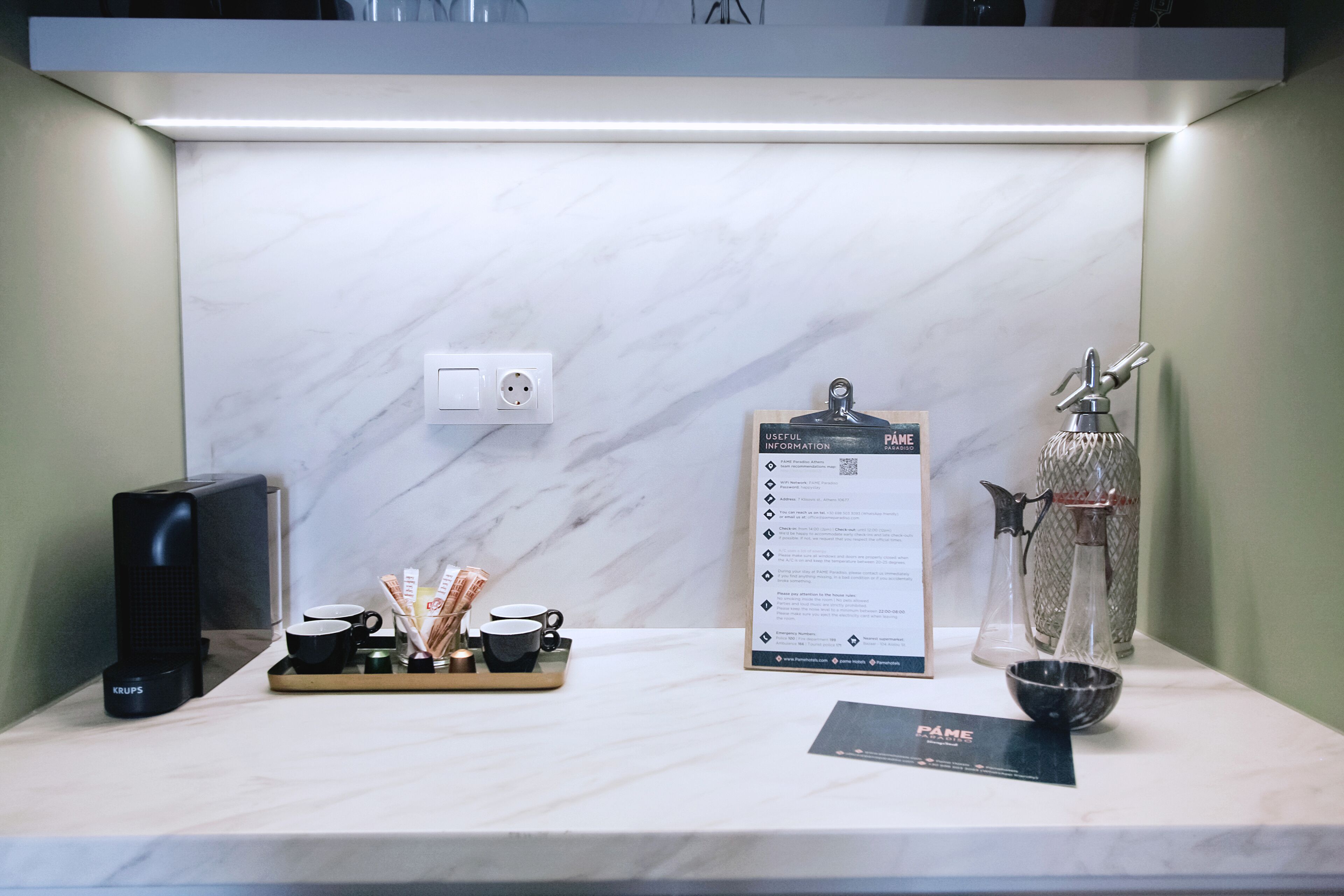A hotel reception desk with a coffee machine, a tray with cups and utensils, a menu board, and a decorative vase.