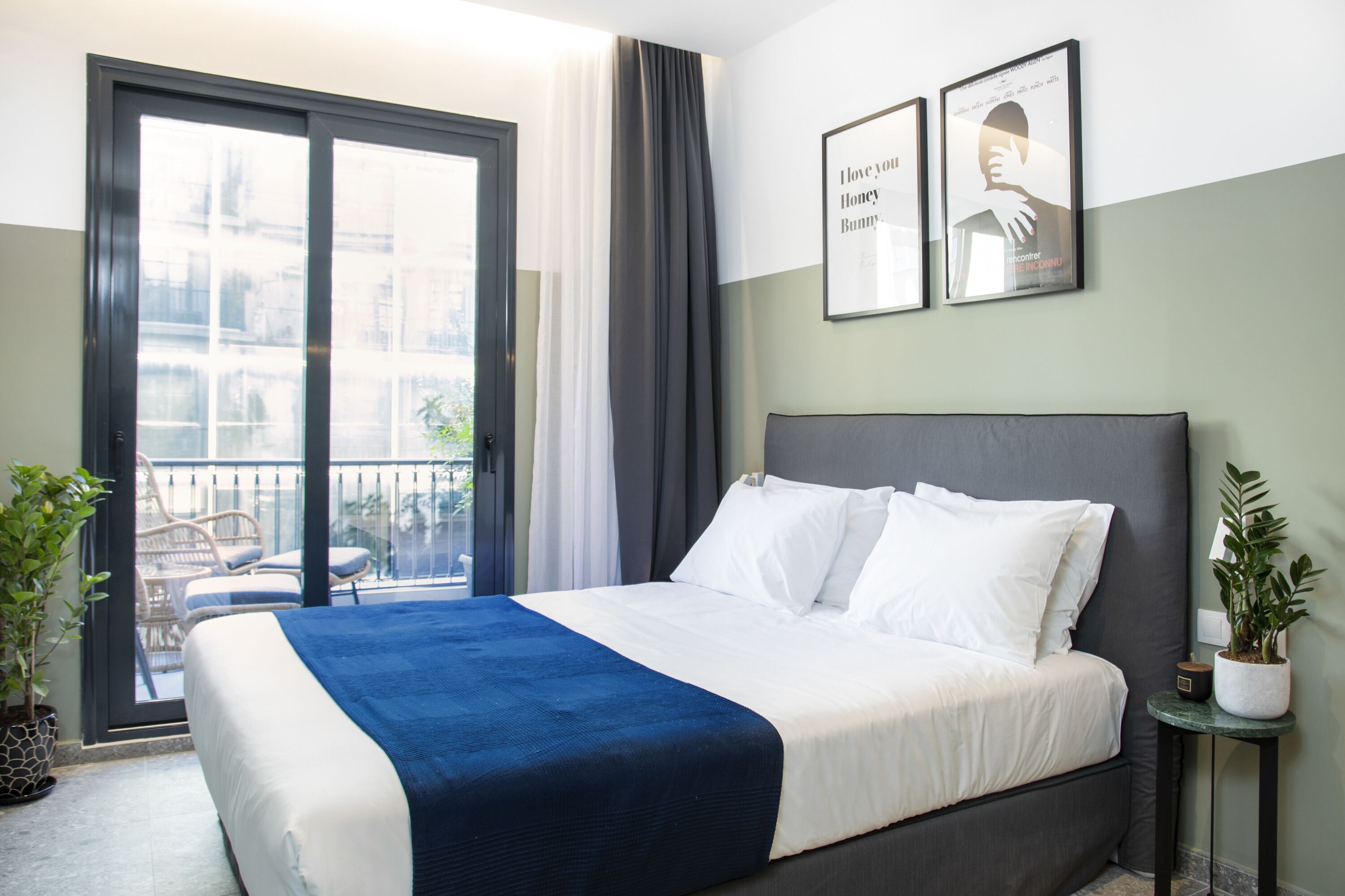 A hotel room with a large bed, a balcony with chairs, and two framed pictures on the wall.