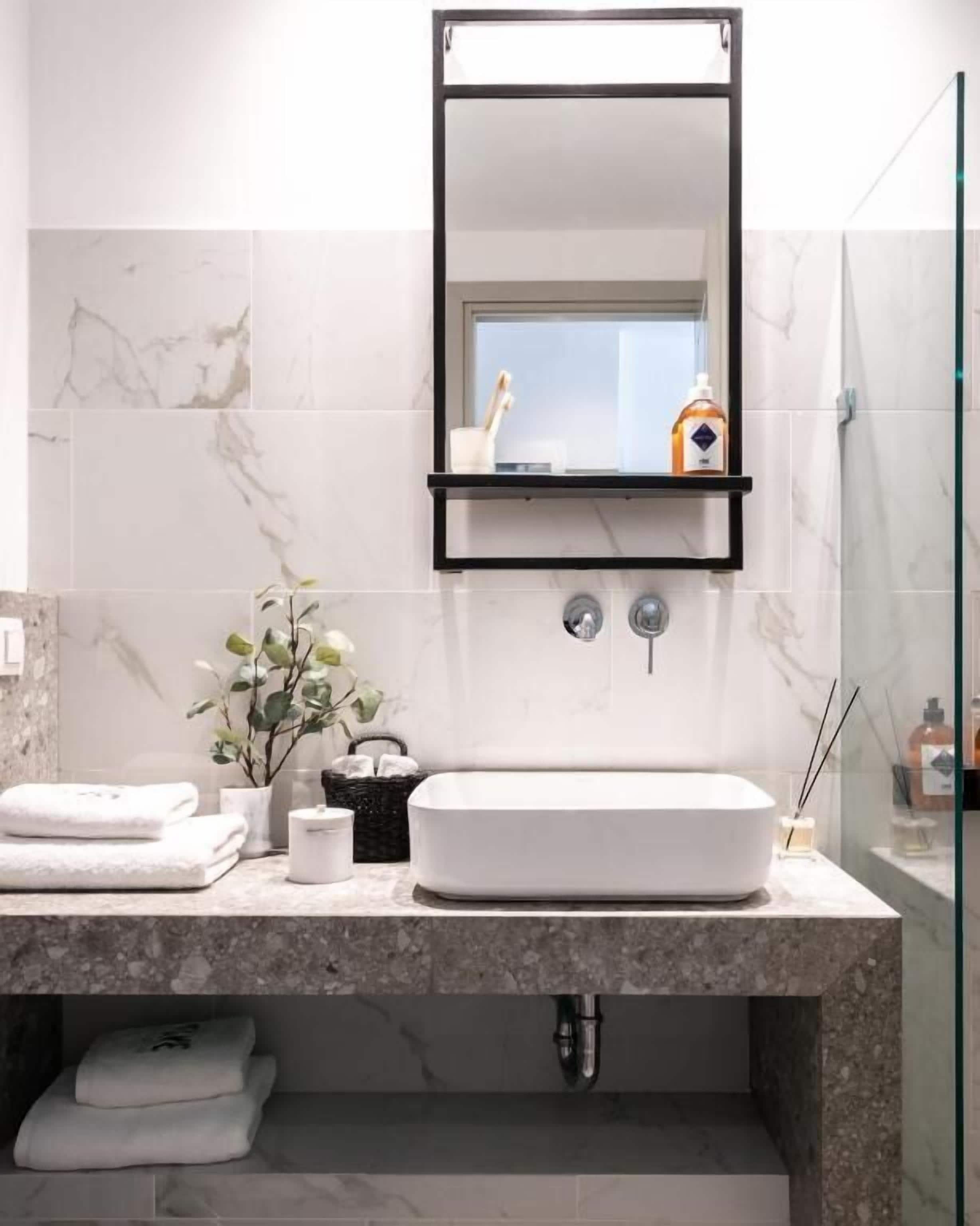 A modern bathroom with a large white sink, a black-framed mirror, and a glass shower enclosure.
