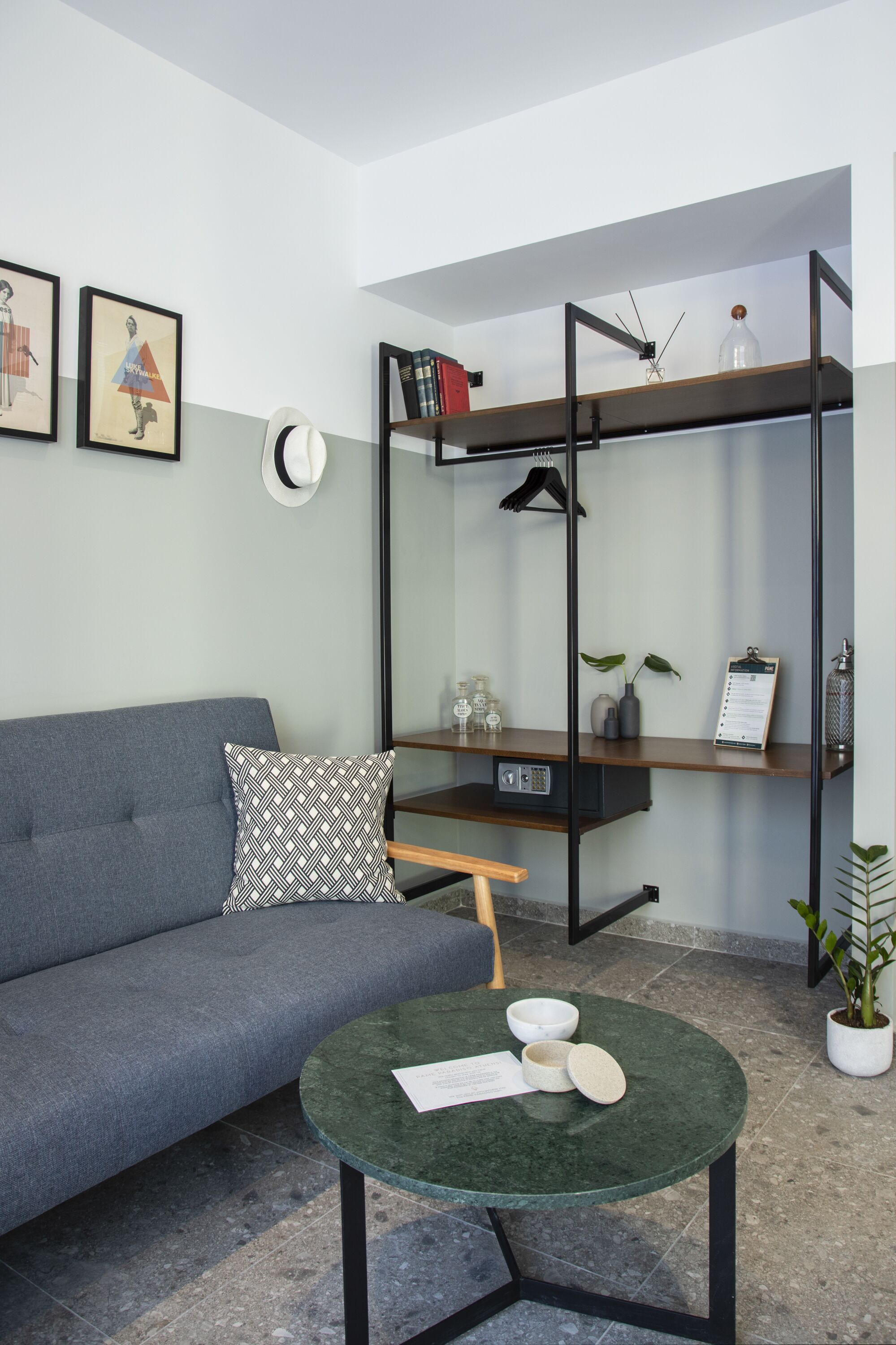 Un salon moderne avec un canapé gris, une table basse ronde verte et une étagère en métal noir adossée au mur.
