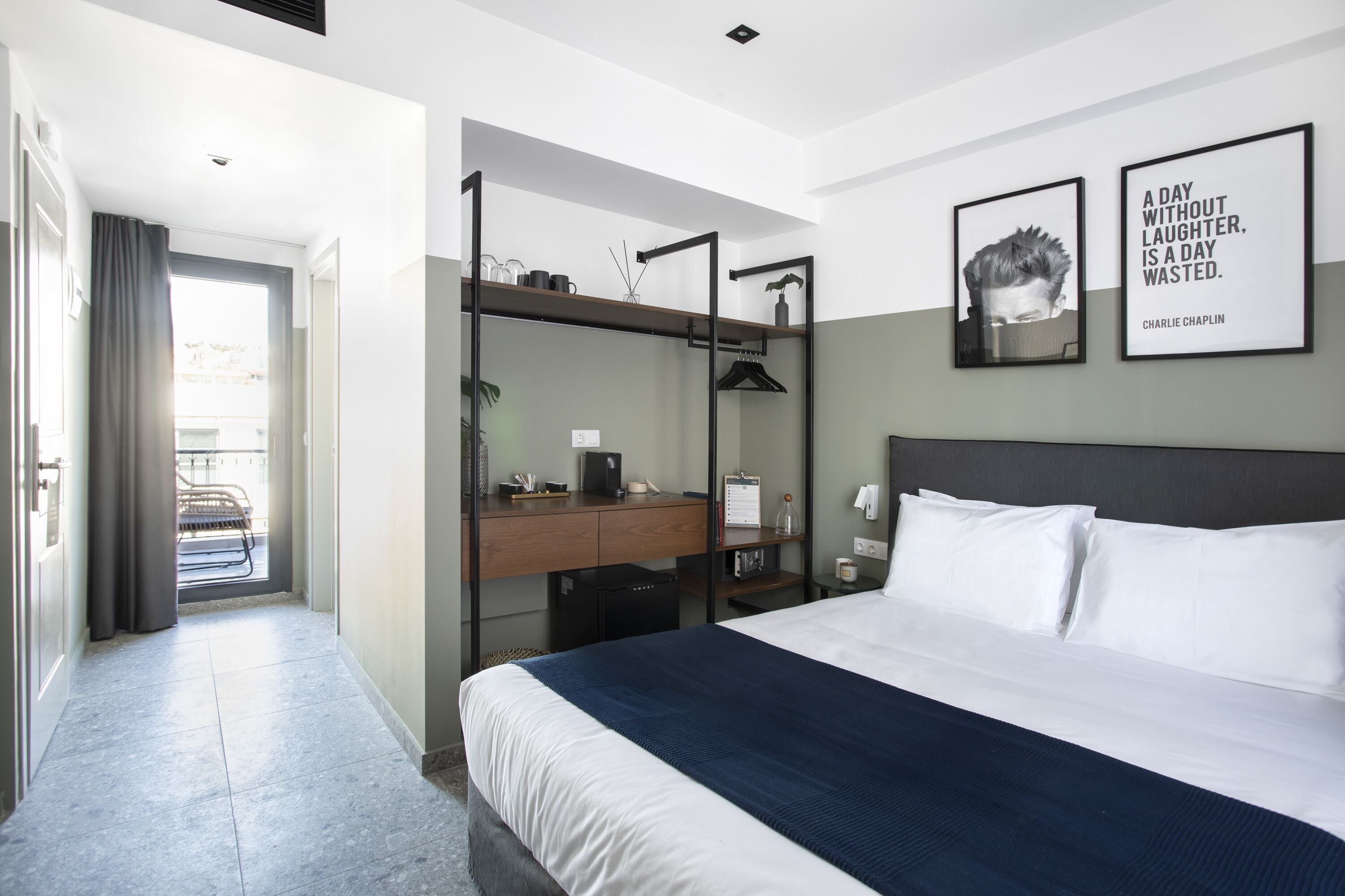 A modern hotel room with a bed, a desk, and a wardrobe. There are two framed quotes on the wall.