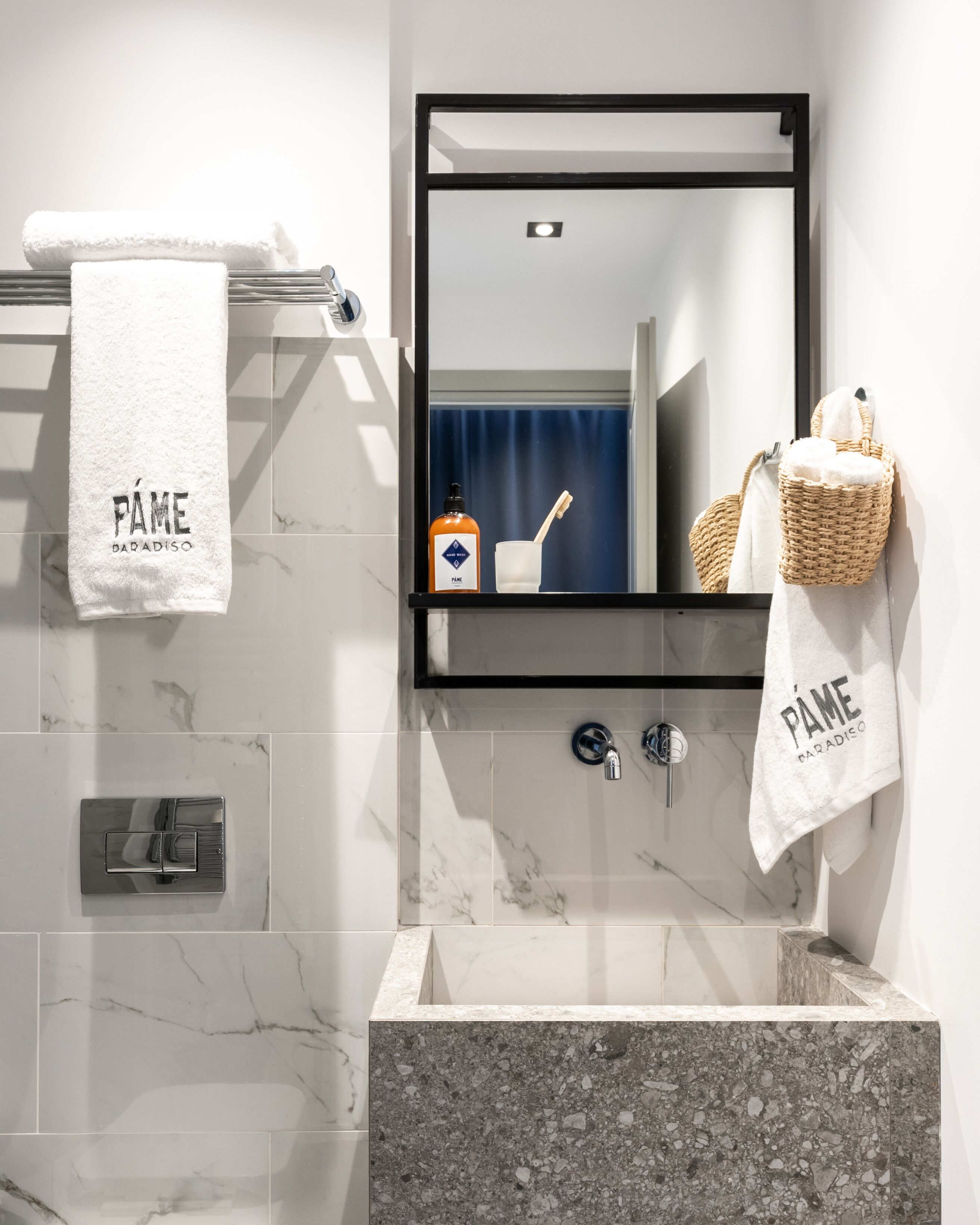 Un baño moderno con un lavamanos de mármol, un espejo y dos toallas colgadas en ganchos.