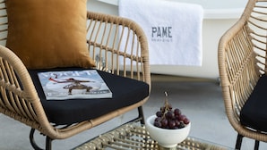 A wicker chair with a magazine and a bowl of grapes, a white bathtub with a towel, and a perforated privacy screen. - Pame Paradiso (Athens)