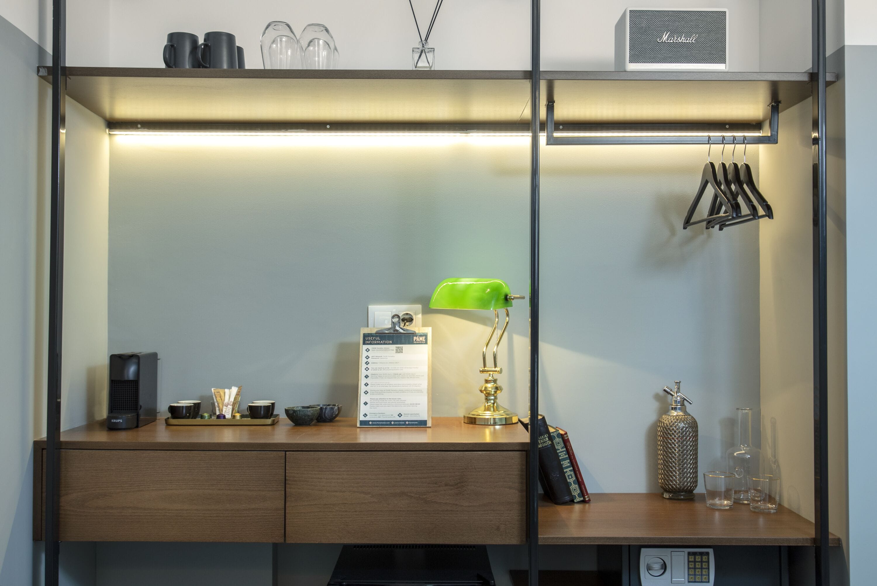 A modern hotel room with a wooden desk, a green desk lamp, a minibar, and a minibar shelf.