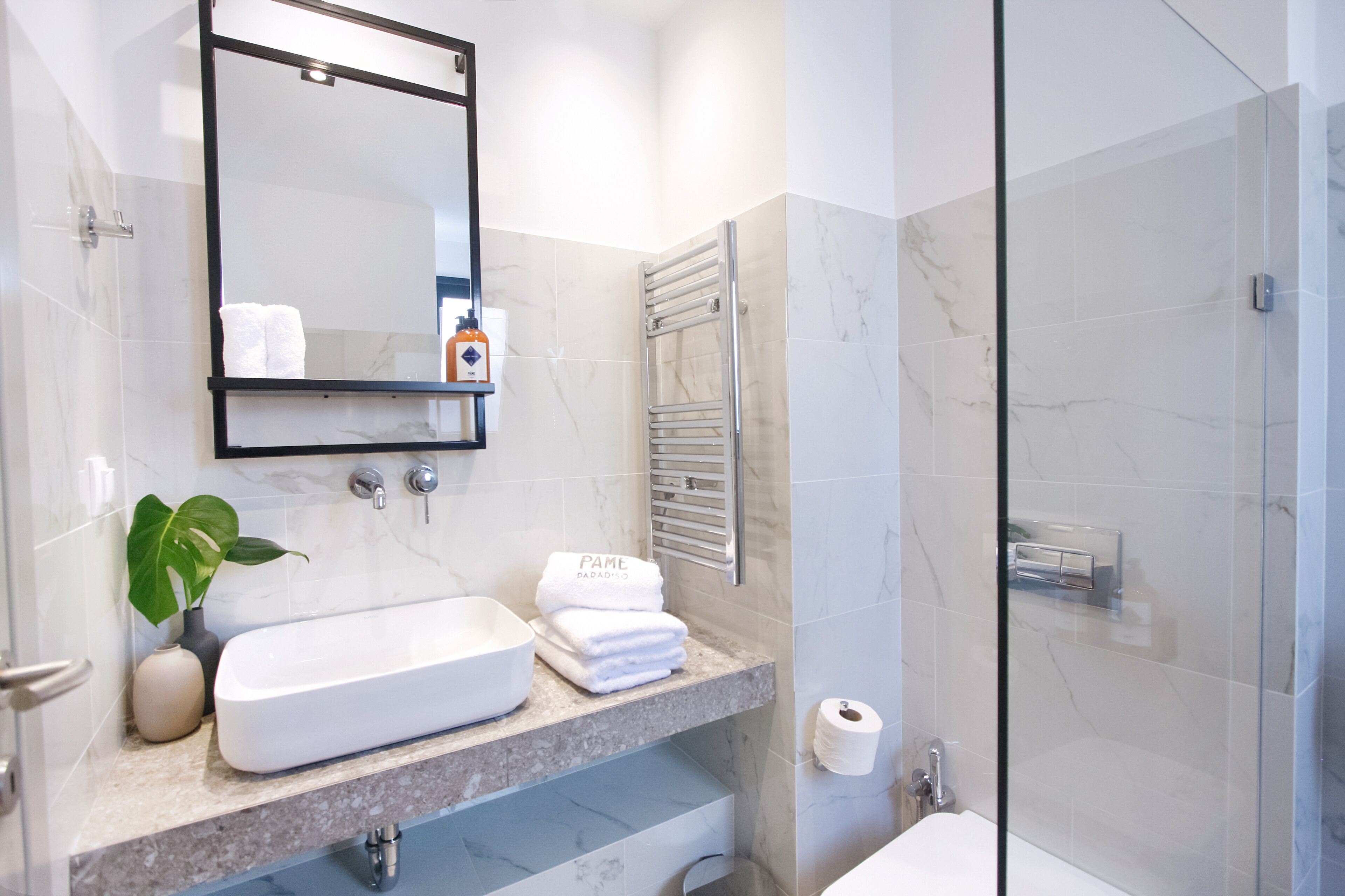 A modern bathroom with a glass shower enclosure, a white sink, and a marble-tiled vanity.