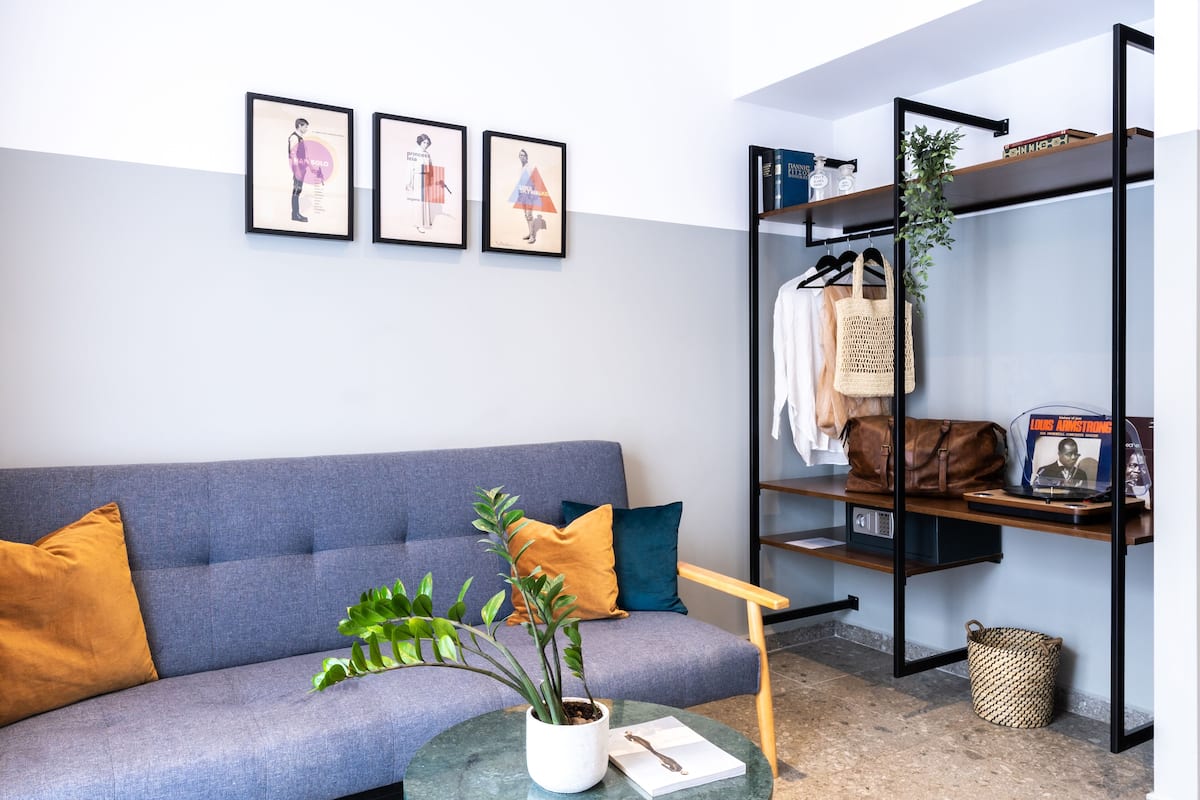 A modern living room with a grey sofa, two cushions, a coffee table with a plant, and a bookshelf with books and a framed picture.