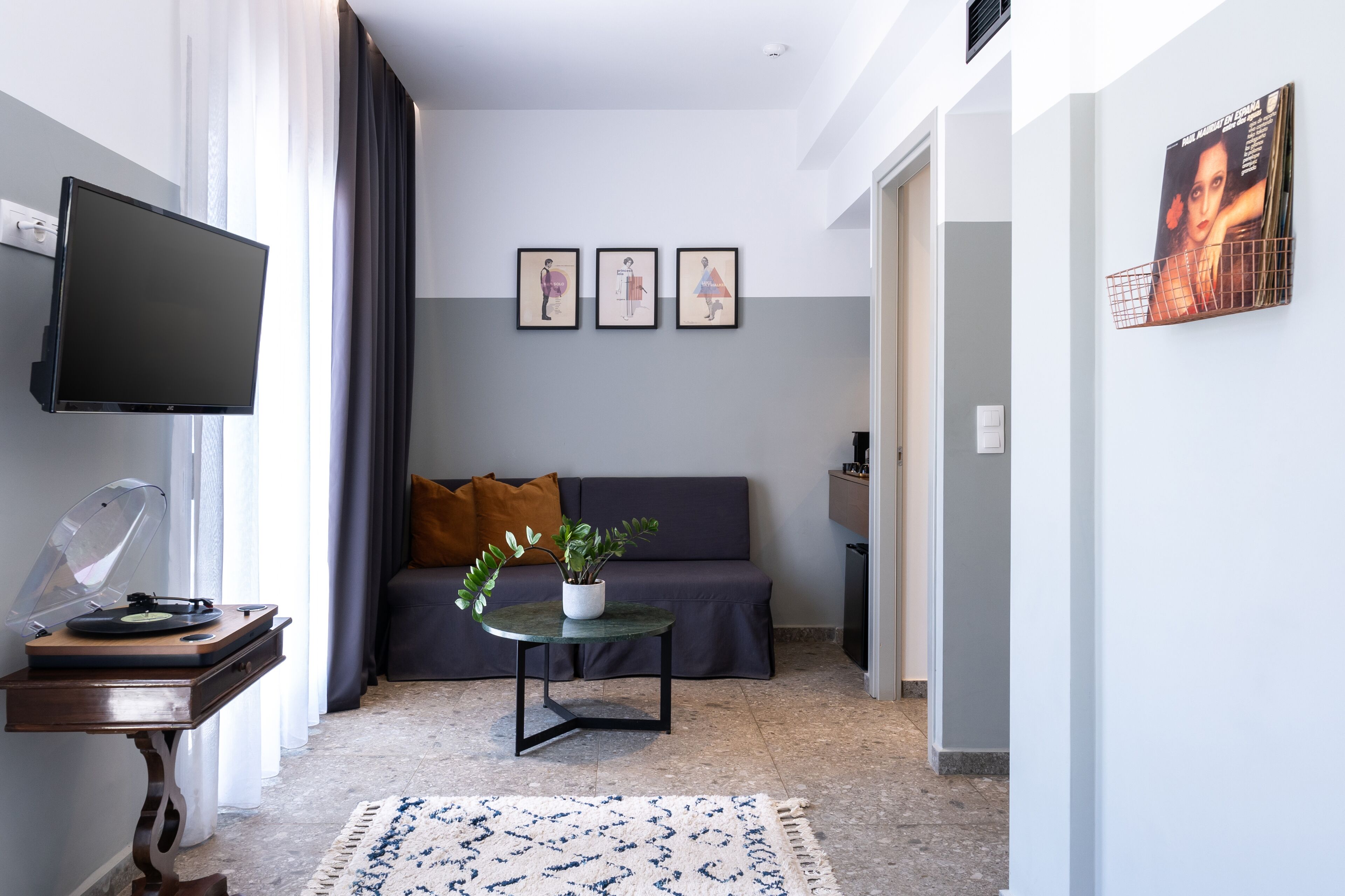 A modern living room with a flat-screen TV, a record player, a sofa with cushions, a small table with a plant, and framed artwork on the wall.