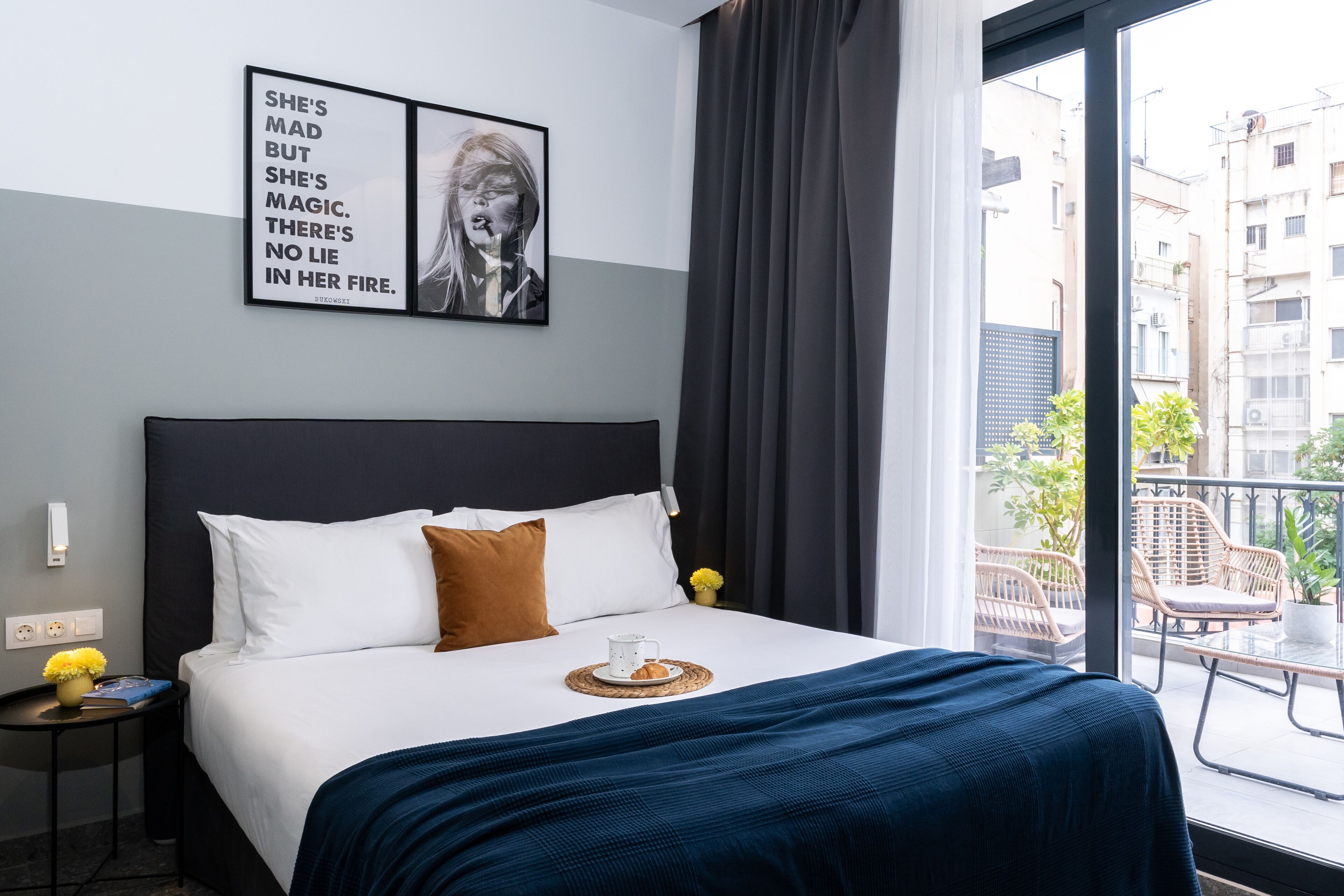Ein Hotelzimmer mit einem großen Bett, Blick auf die Stadt durch das Fenster und einem motivierenden Zitat an der Wand.