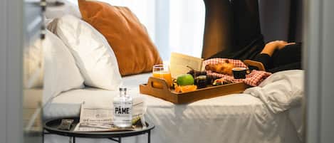 A hotel room with a bed, a bedside table with a newspaper, a tray with food and drinks, and a window with curtains.