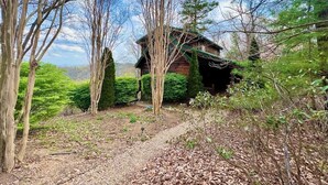 A rustic cabin surrounded by trees and a gravel path. - Bear Necessities - Hot tub, View, Spectacular! (Ferguson)