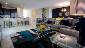 En moderne stue med sofa, stole, et glasbord og en trappe til øverste etage.