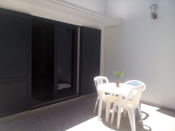 A patio with a white table and chairs, a small potted plant, and a sliding door.