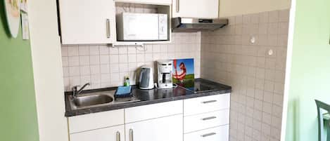 Une cuisine de taille réduite, avec des meubles blancs, un four à micro-ondes, une machine à café et un évier.