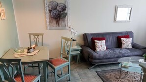 Una sala de estar con un sofá gris, almohadas rojas y blancas, una mesa de centro de vidrio y un comedor con una mesa y sillas.