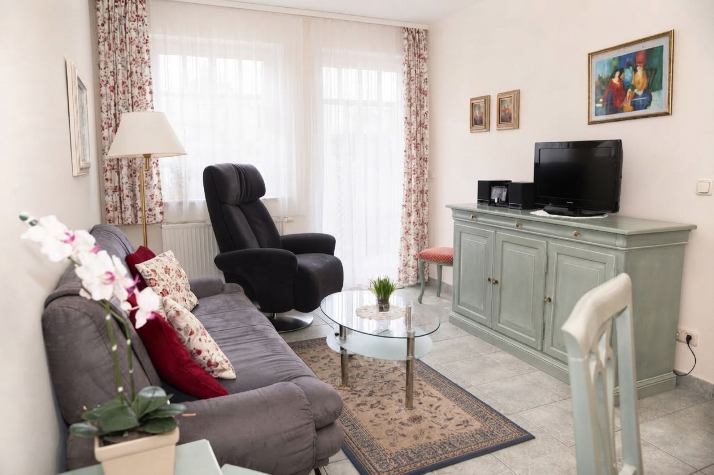 A living room with a sofa, armchair, glass coffee table, and a television on a cabinet.