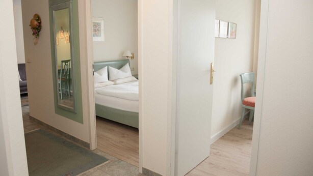 Un dormitorio con una cama, una silla y una puerta que da a otra habitación.