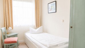 Un dormitorio pequeño y ordenado con una cama individual, una silla, un escritorio y una ventana con cortinas.