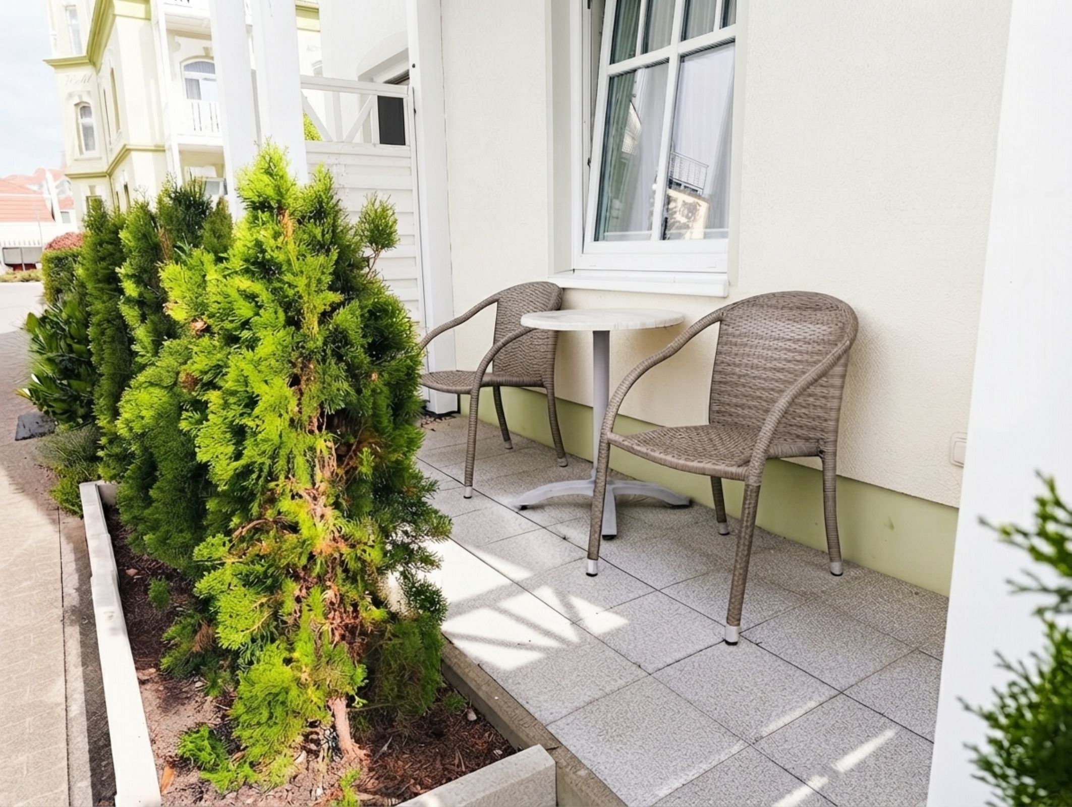 A patio area with a small garden bed, two wicker chairs, and a table.