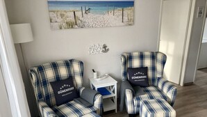Ett rum med två fåtöljer i rutigt tyg och en tillhörande pall, ett litet vitt sidobord och en tavla med strandmotiv på väggen.