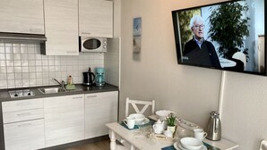 Ett modernt kök med vita skåp, en mikrovågsugn och en kaffebryggare. Ett matbord med vita stolar är dukat med tallrikar och en vattenkokare.