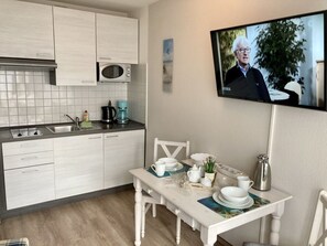 A modern kitchen with white cabinets, a microwave, and a coffee maker. A dining table with white chairs is set with dishes and a kettle.