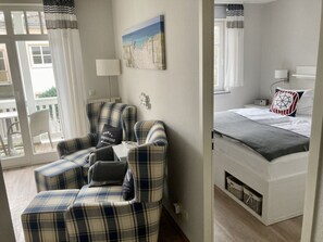 Una habitación con cama, una silla, una mesa y un cuadro en la pared.