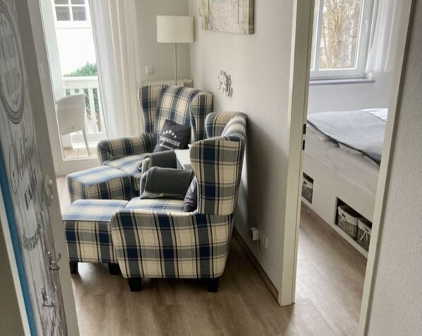 A corner sofa with plaid upholstery, a lamp, and a window with a view of trees.