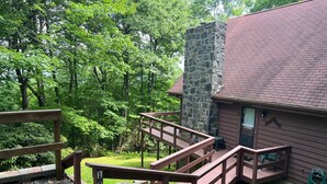 A wooden deck leading to a stone building with a red roof, surrounded by lush greenery.