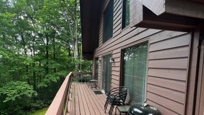 A wooden deck with a grill and chairs, overlooking a forested area.