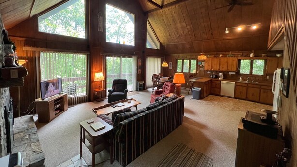 A spacious living area with a high ceiling, large windows, a fireplace, a dining area, and a kitchen.