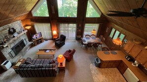 A spacious cabin interior with a stone fireplace, a dining area, and a kitchen.