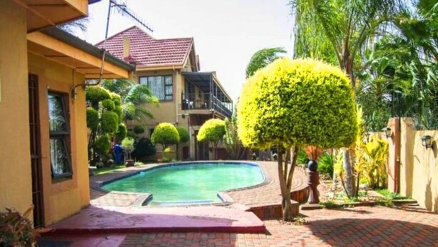 A swimming pool surrounded by a brick patio, a yellow building, and well-maintained greenery. - Comfit Zone B&B (Newcastle)