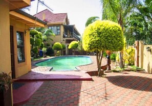 A swimming pool surrounded by a brick patio, a yellow building, and well-maintained greenery. - Comfit Zone B&B (Newcastle)