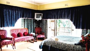 A room with a bed, two armchairs, a small table, a television, and a window with curtains. - Comfit Zone B&B (Newcastle)
