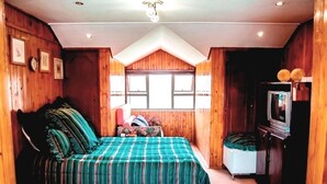 A cozy room with wooden walls, a bed with a striped bedspread, a small white bedside table, and a television on a wooden stand. - Comfit Zone B&B (Newcastle)