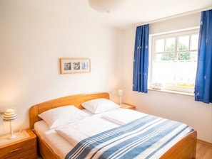 A bedroom with a bed, bedside tables, a lamp, a window with curtains, and a wall-mounted picture.