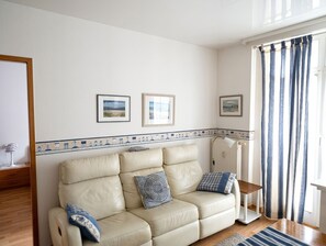 A living room with a beige sofa, two framed pictures on the wall, and a window with curtains.